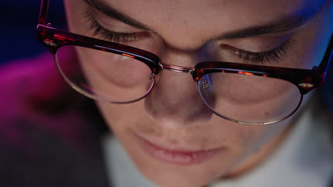 close up young business woman working late using computer browsing online looking at information on screen wearing glasses top view