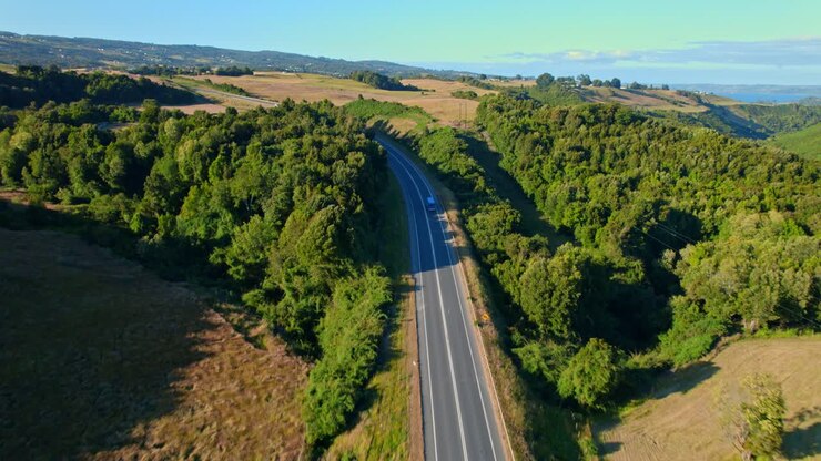 Inseguimento di un'auto blu su strada panoramica attraverso il paesaggio verde del Cile, riprese aeree con drone 4K a Chiloé