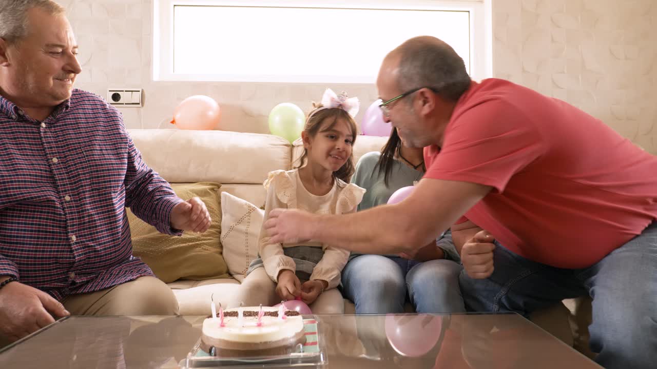 Girl blowing out birthday candles with her gay grandparents and mother at home