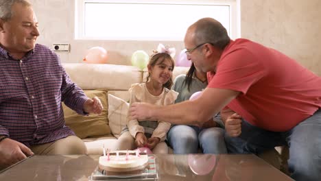 girl blowing out birthday candles with her gay grandparents and mother at home