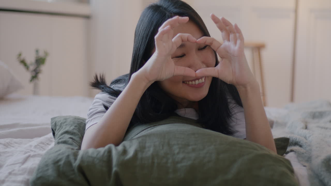 Woman making heart shape with hands on bed