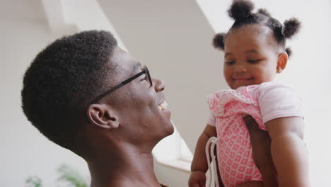 father playing game with baby daughter and lifting her in air in loft apartment