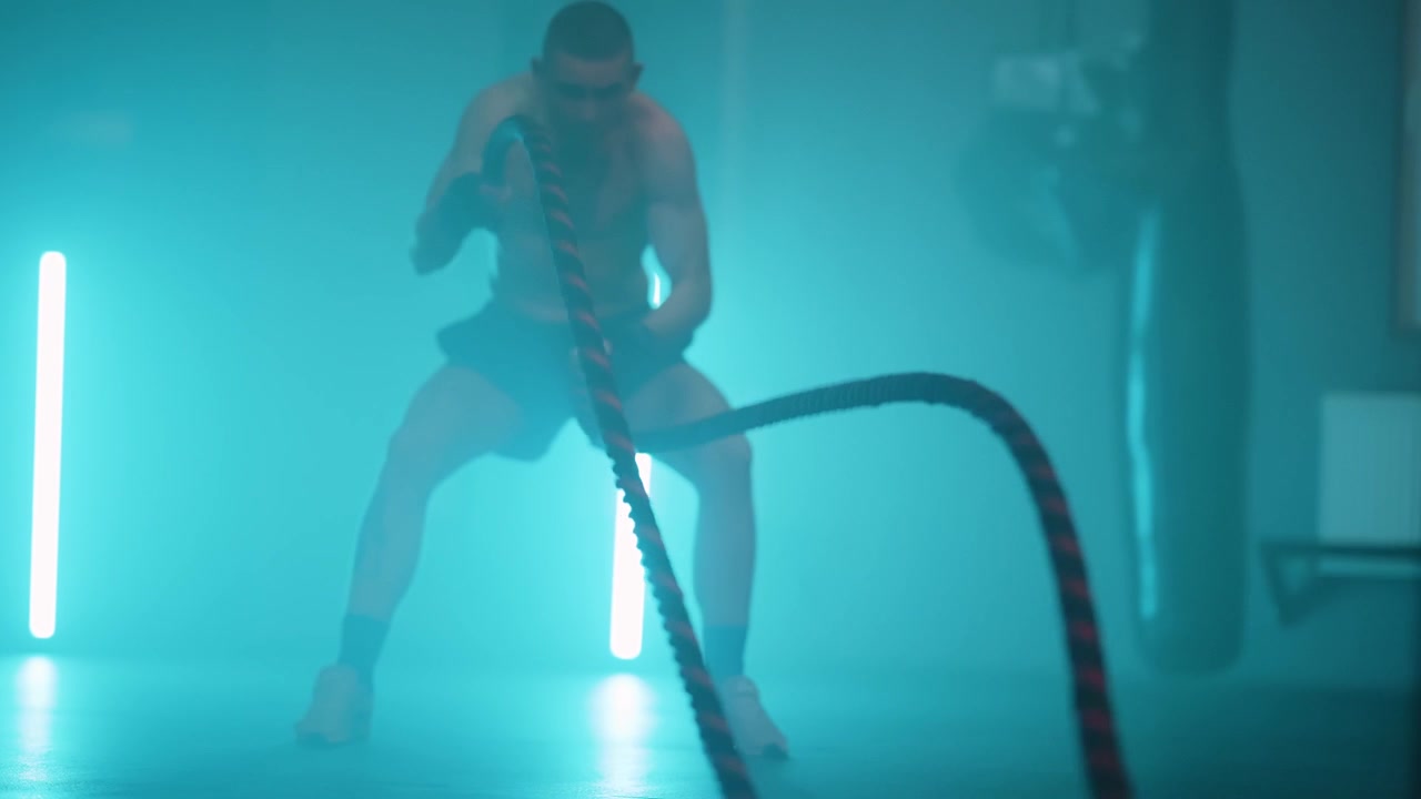 Muscular Man Training with Battle Ropes in a Neon Lit Gym