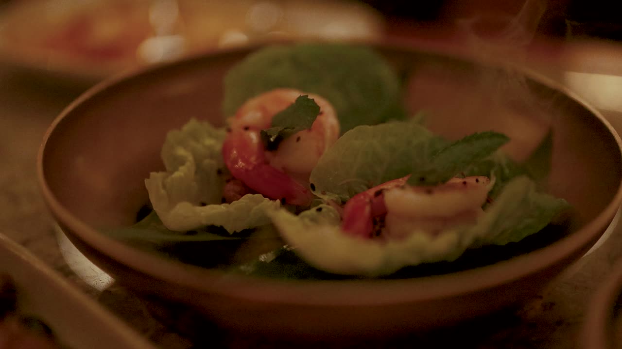 A close-up of a shrimp Miang Kham dish on a wooden plate, captured in warm, ambient lighting
