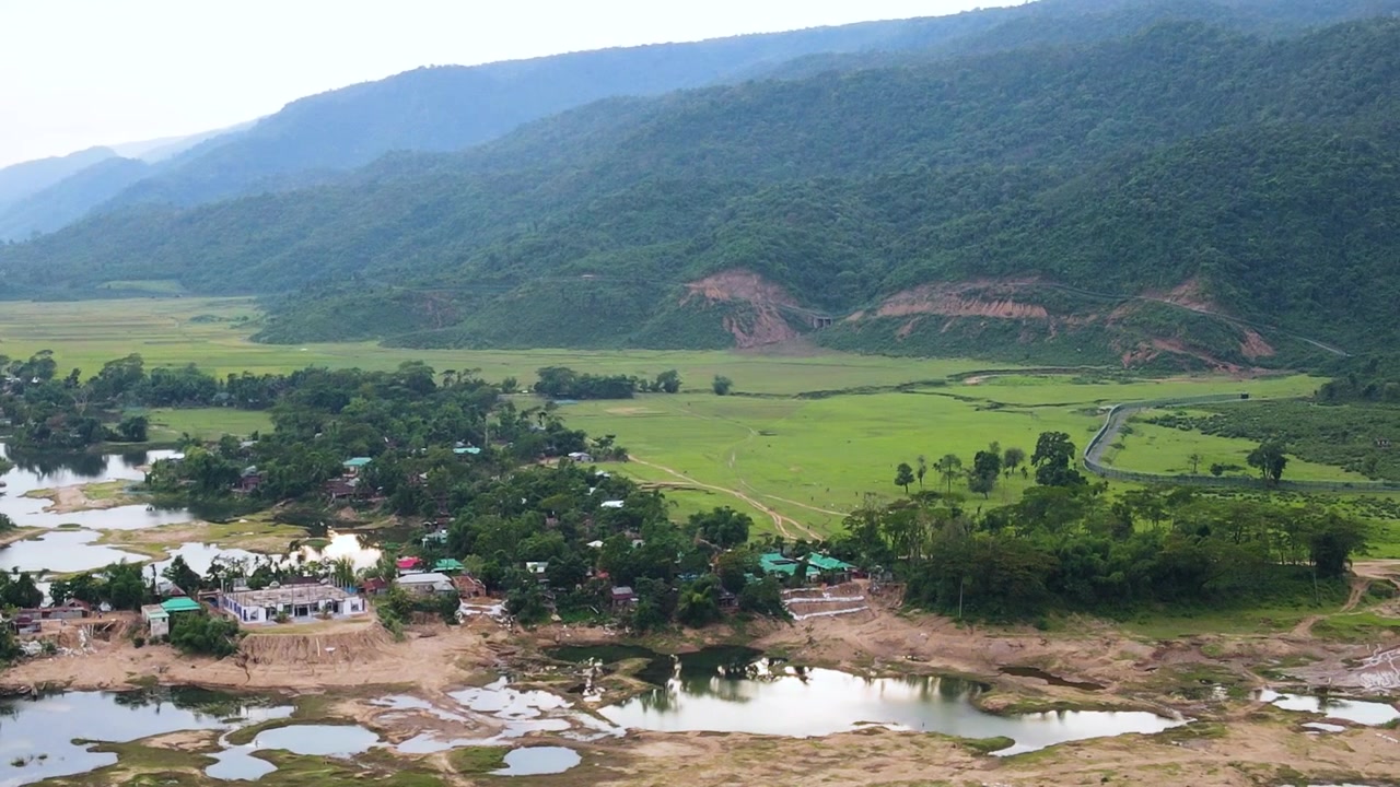 Đồng ruộng và làng mạc, khu định cư nông thôn và vùng đất ngập nước nép mình dưới những ngọn đồi Meghalaya tươi tốt gần khu vực biên giới Bangladesh-Ấn Độ, bầu trời mờ ảo, ban ngày, cảnh quay drone trên không góc rộng từ trên cao