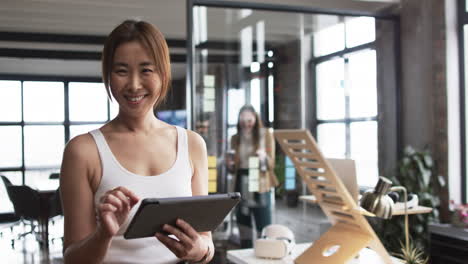 una mujer de negocios asiática con una camiseta blanca sostiene una tableta, sonriendo a la cámara