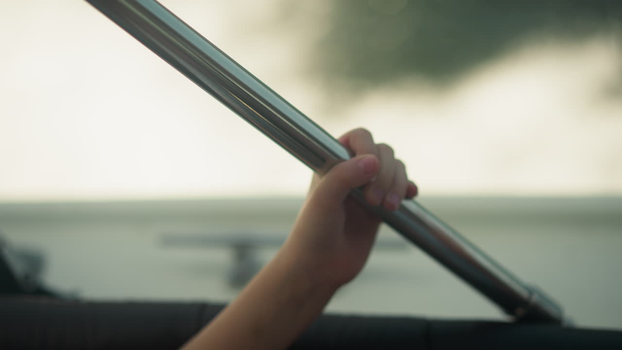 작은 아이의 손은 금속 바를 들고 모터 보트를 타고 여행합니다. 여름 휴가 동안 안전 장비와 함께 요트를 타고 있습니다. 관광 활동.