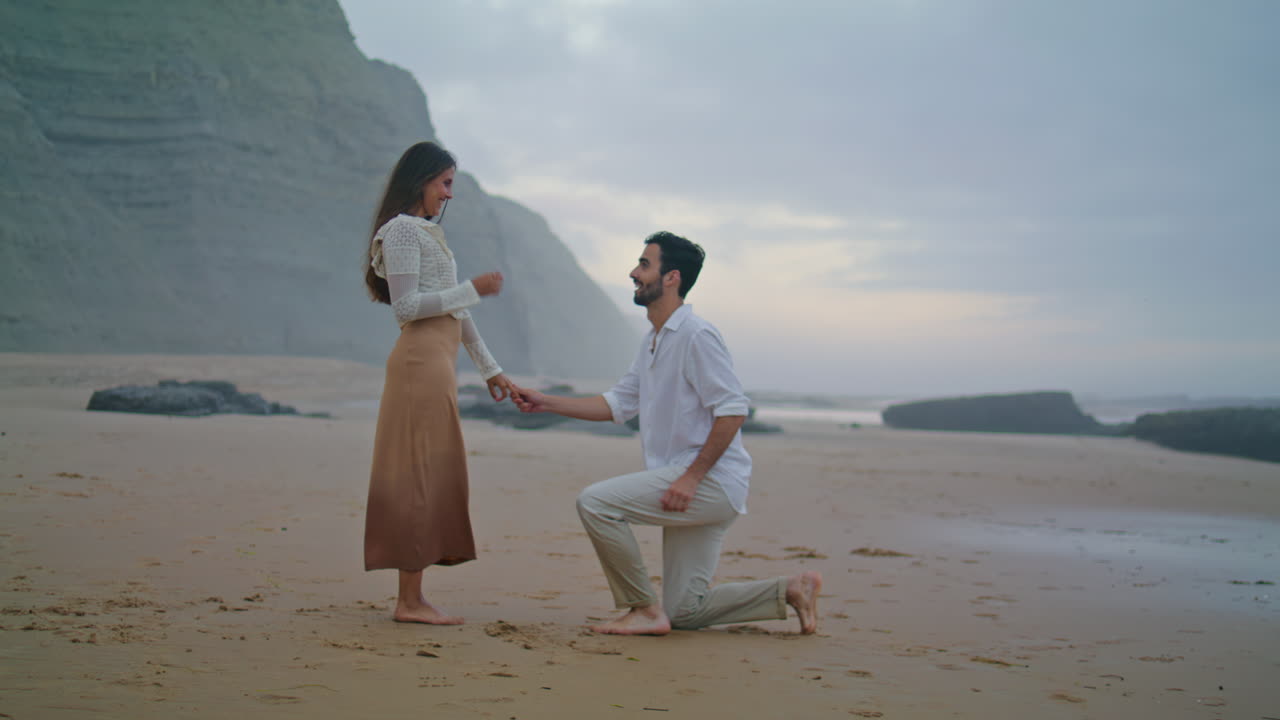 로맨틱한 남자가 해변에서 여자에게 결혼을 제안합니다. 약혼을 축하하는 커플