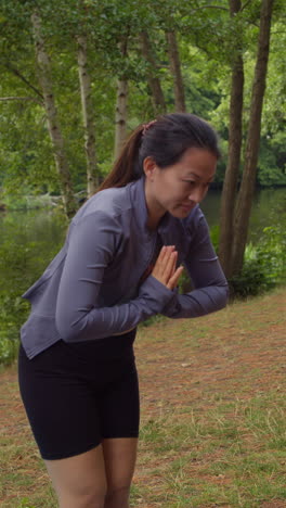 Video-Vertical-De-Una-Mujer-Vestida-Con-Ropa-Deportiva-Haciendo-Estiramientos-De-Yoga-Sobre-Una-Colchoneta-En-Un-Bosque-Junto-A-Un-Lago-O-Río-Disfrutando-De-La-Paz-Y-La-Belleza-De-La-Naturaleza-Filmado-En-Tiempo-Real