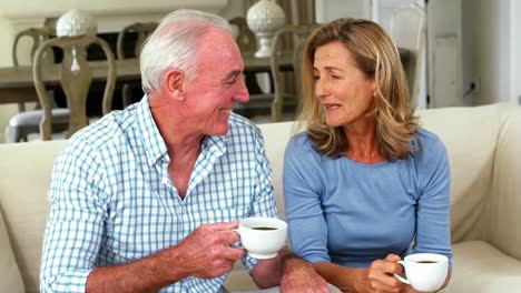 Lächelndes-älteres-Paar-Interagiert,-Während-Es-Im-Wohnzimmer-Eine-Tasse-Kaffee-Trinkt