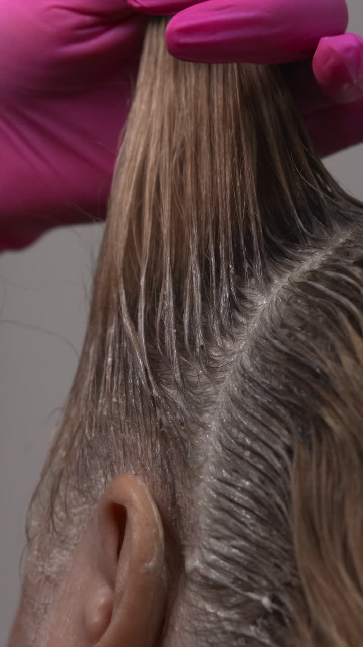 Primo piano: pettinatura di capelli biondi sezionati con mano di stilista guantata di rosa, profilo di cliente caucasica, riga pulita.