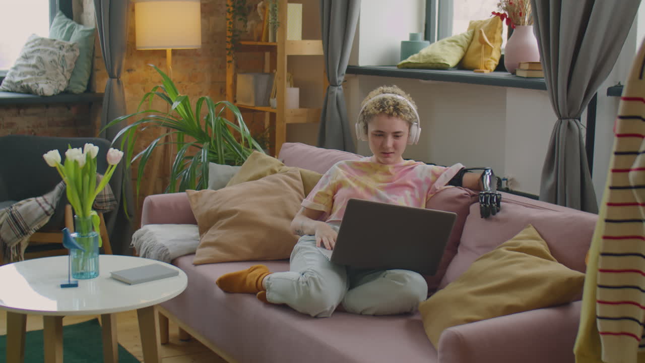 Girl with Prosthetic Arm in Headphones Using Laptop at Home