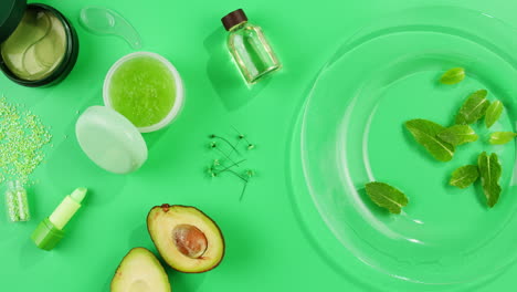 Fresh ripe avocados with cream and essential oil on green background with mint mentol, make up cosmetics