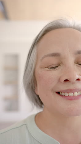 vertical video: smiling elderly woman with closed eyes enjoying peaceful moment at home