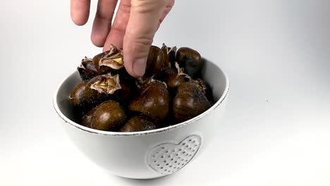 a hand picking up a roasted chestnut from a white ceramic bowl, still, isolated, slomo