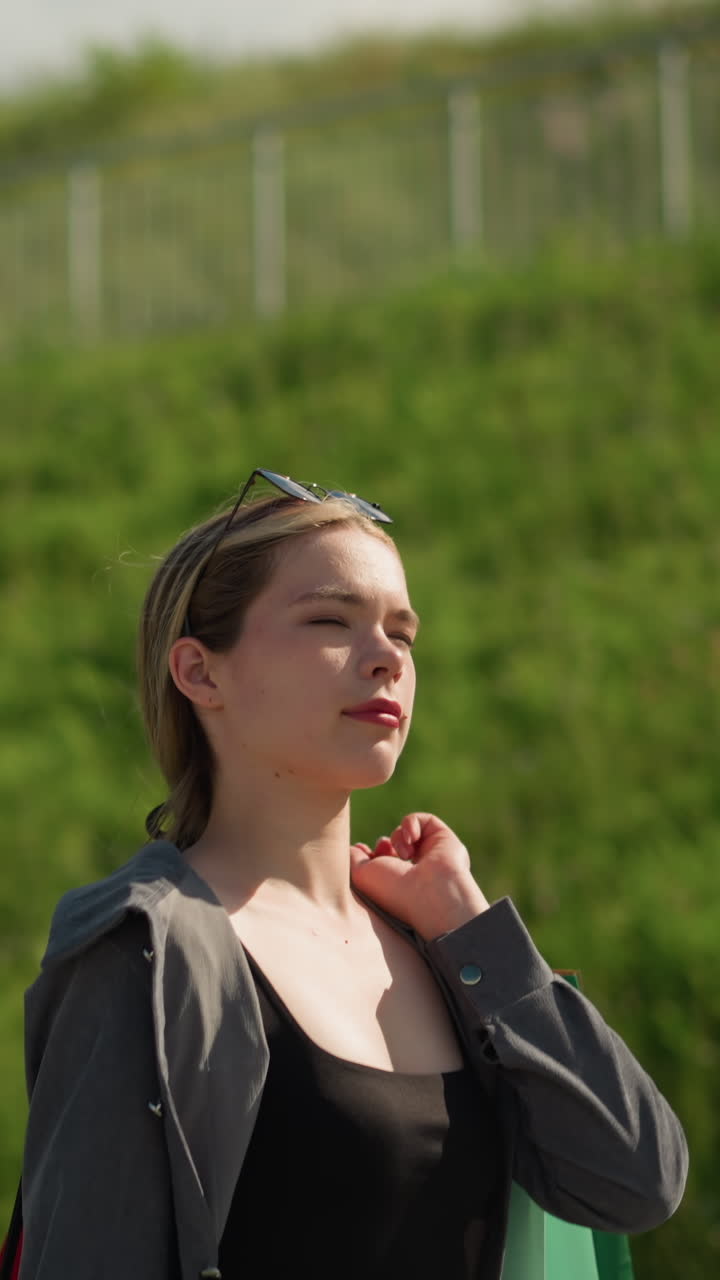 철 철로와 초록색으로 언덕 근처를 는 여성, 그녀의 어깨에 뒤로 쇼핑 가방을 들고, 검은 을 드러내는 열린 셔츠를 입고, 울창한 녹색 언덕의 배경