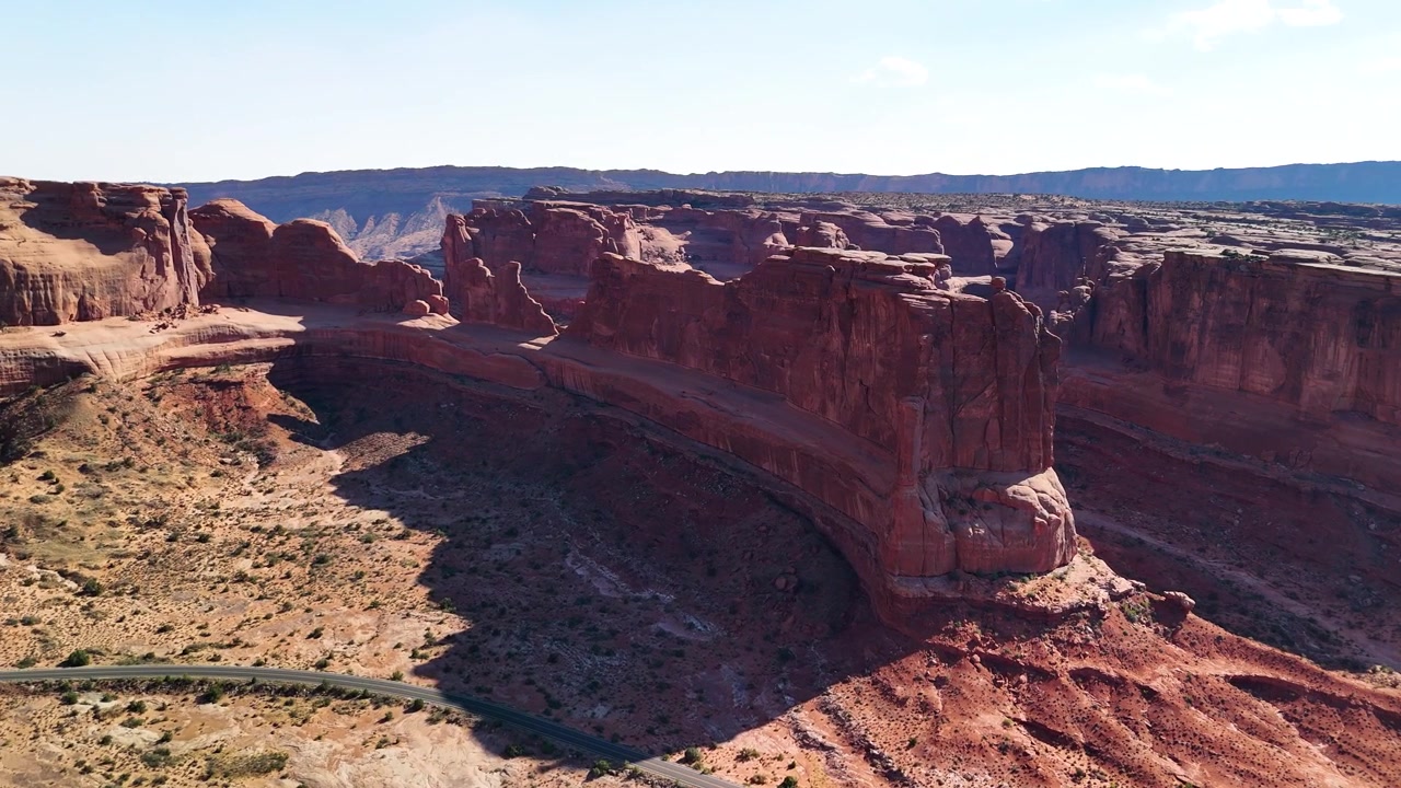 Splendido filmato stock del Parco Nazionale di Arches, USA, durante un pomeriggio luminoso. La luce solare brillante illumina le maestose strutture di arenaria rossa e il paesaggio desertico sotto un cielo azzurro limpido.