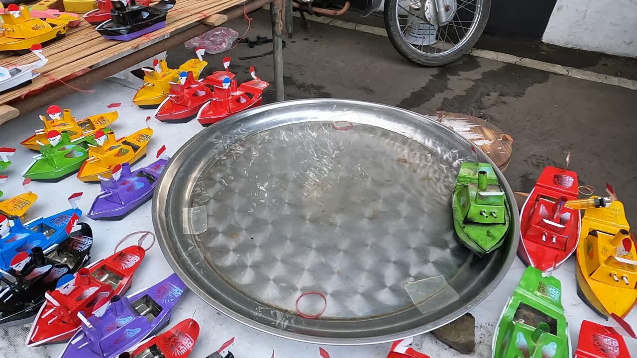 Steam-powered toy boat moves on metal bowl outdoors in Indonesia