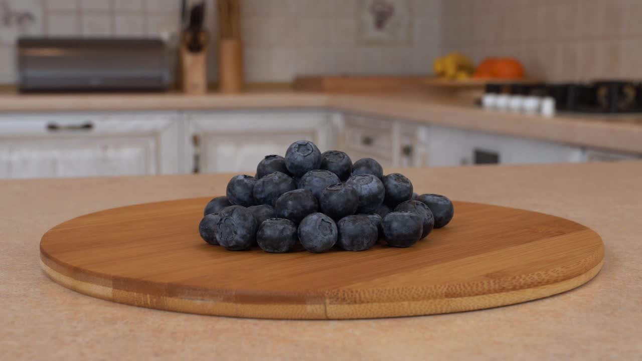 대나무 접시 위에 여러 개의 블루베리 베리. 배경에 색 주방을 가진 회전 카메라. dolly-shot.