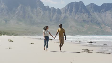 afrikanisch-amerikanisches paar hält sich an den händen und geht am strand