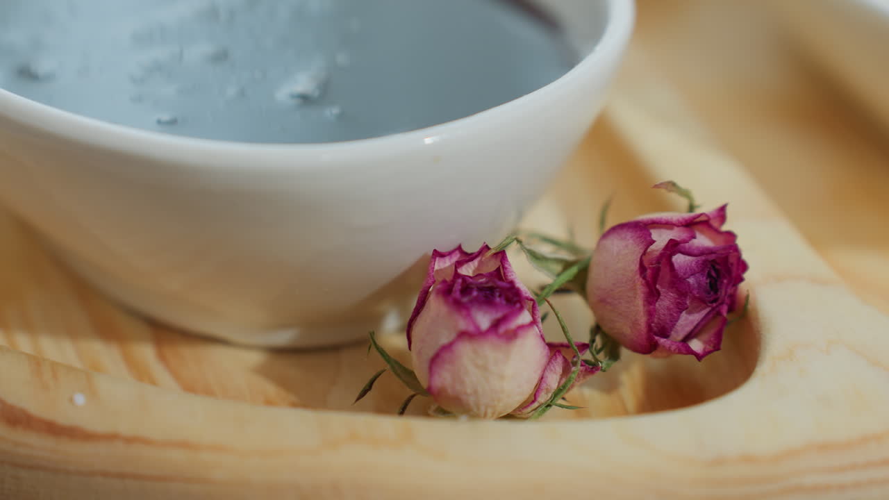 Primo piano di una tazza bianca piena di miele, posizionata su un vassoio di legno con delicati fiori secchi; l'illuminazione soffusa esalta l'estetica calda e rustica, creando una composizione alimentare accogliente e artistica
