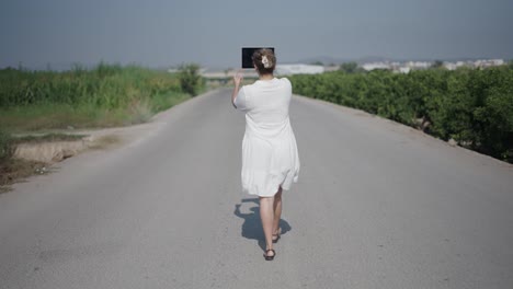 woman walking on country road with tablet