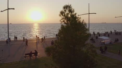 Antena---Plano-Bajo-De-Gente-Caminando-Por-El-Paseo-Marítimo-De-Tesalónica-Al-Atardecer