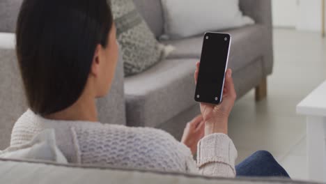 back view of asian woman sitting on sofa, resting with smartphone with copy space at home