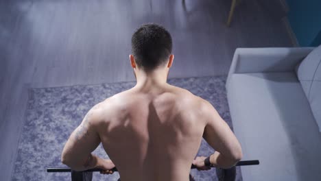 bodybuilder man working out at home using weights for back and arm muscles.