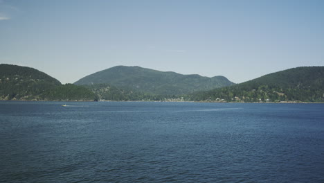 Approaching-Bowen-Island-by-sea,-a-speedboat-is-crossing-in-the-distance