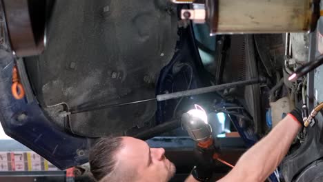 mechanic working on a car's underside with a flashlight