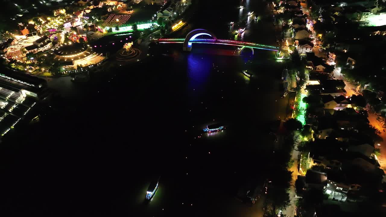 Colorful bridge at night with boats on water and lively street lights in Hoi An