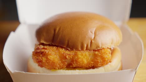 revealing fried fish burger in soft bun with mayonnaise and cheese, closeup