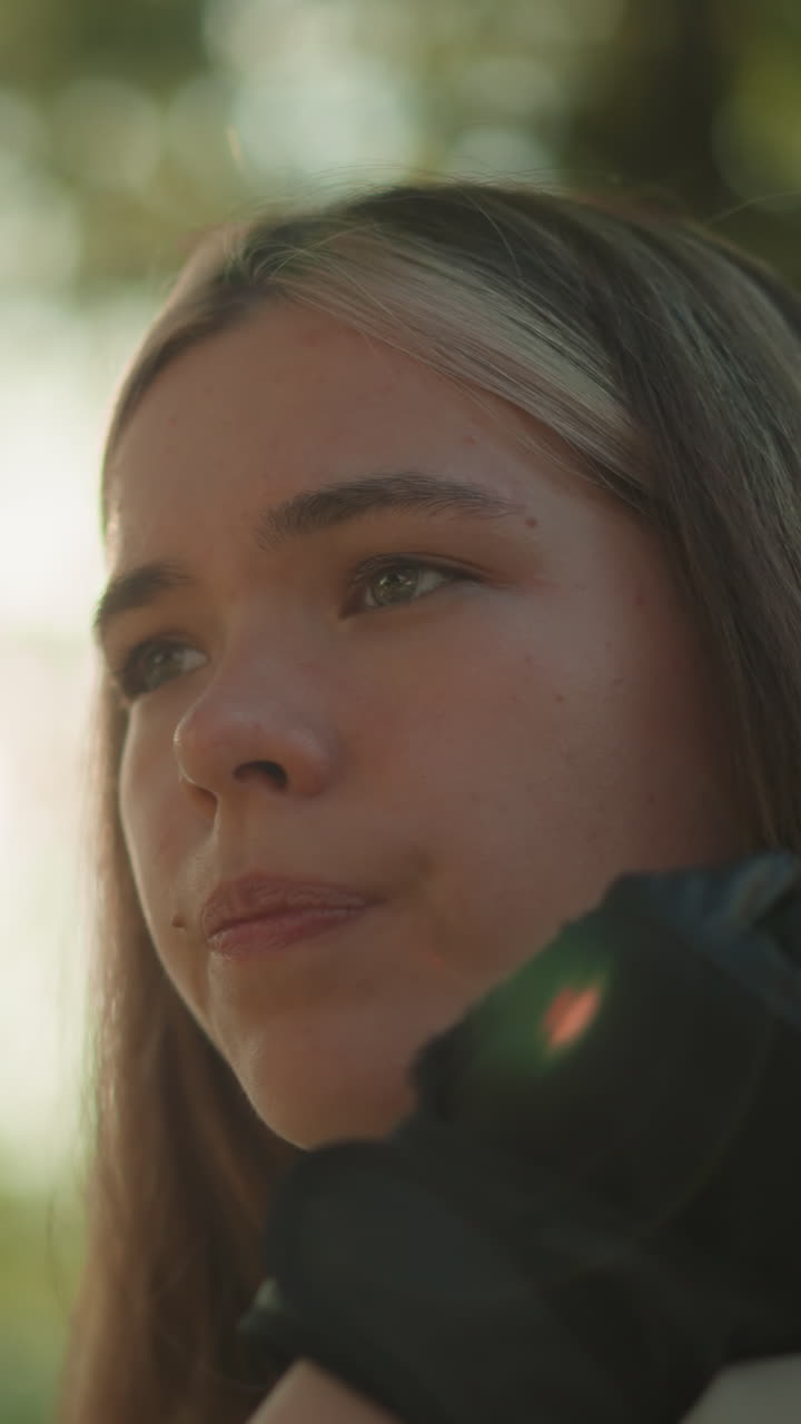hermosa mujer joven descansando el mentón en su mano, mirando pensativo en la distancia, la luz del sol crea un efecto de halo cálido a su alrededor mientras la vegetación borrosa