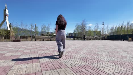 A-woman-walks-across-a-brick-square-with-a-large-monument-in-the-distance