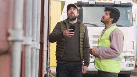 Boss-And-Worker-Organizing-A-Truck-Fleet-In-A-Logistics-Park-While-They-Watching-Something-On-A-Smartphone