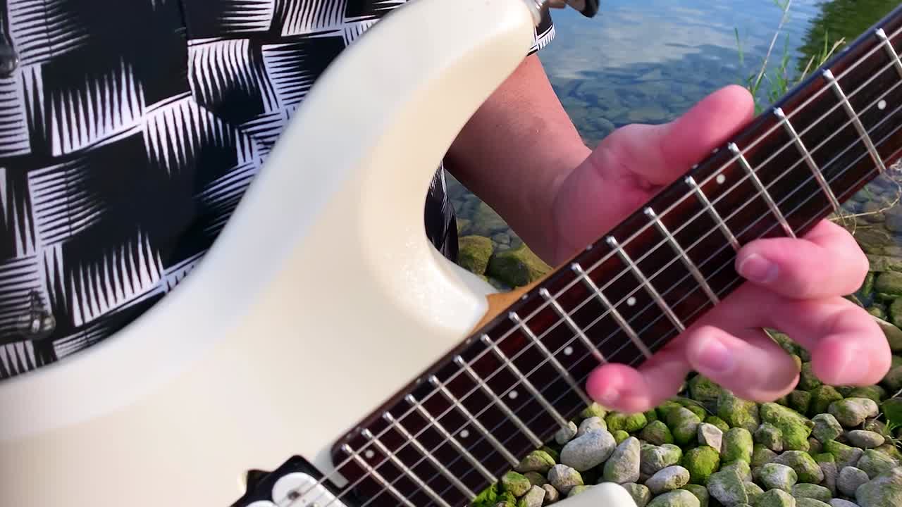 un guitarrista masculino toca una guitarra blanca junto al lago