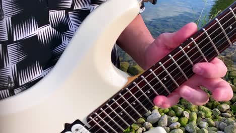 a male guitarist plays a white guitar by the lake