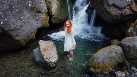 a red-haired girl in a white dress enters a small waterfall