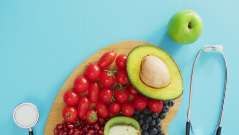 Video-of-stethoscope-and-fresh-fruit-and-vegetables-on-heart-shaped-wooden-board-on-blue-background