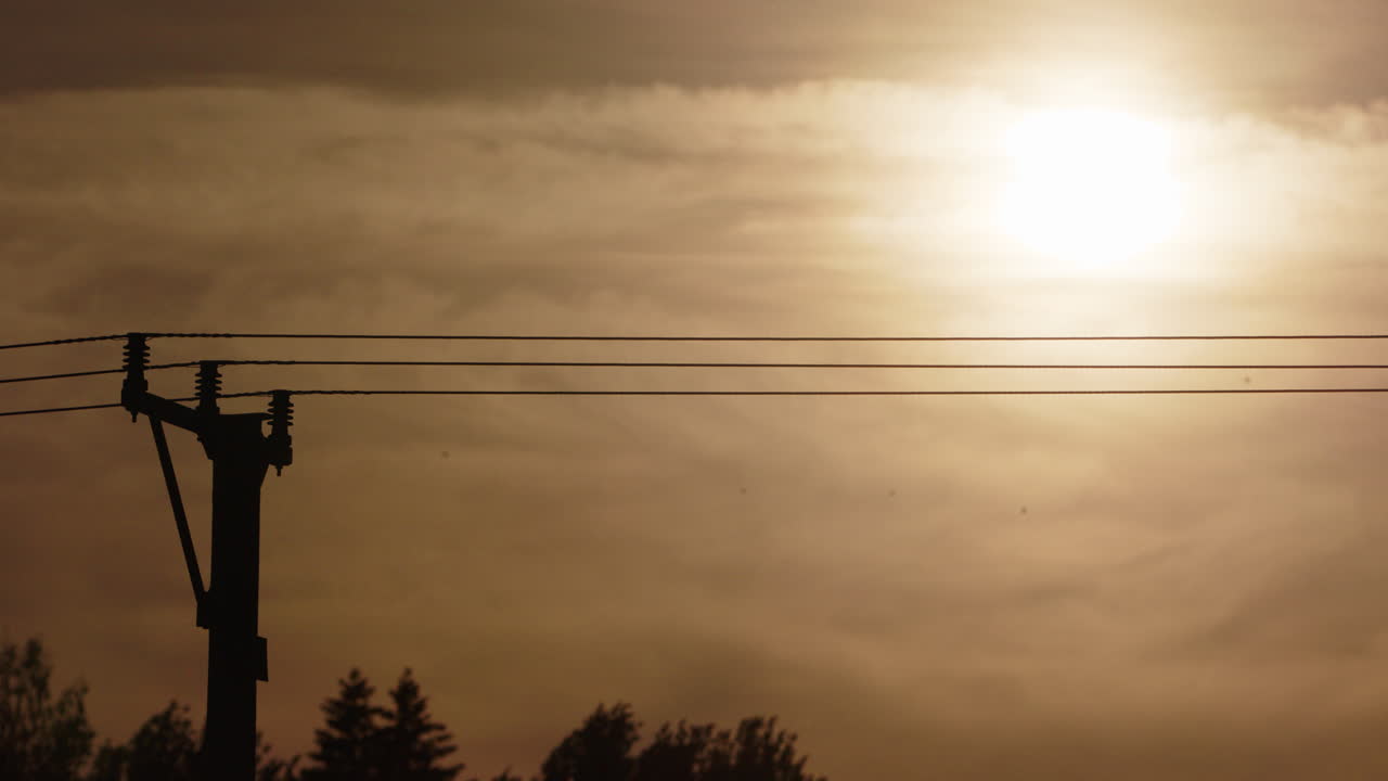 silhouette di linee elettriche contro il vivo cielo arancione dell'ora d'oro, telefoto