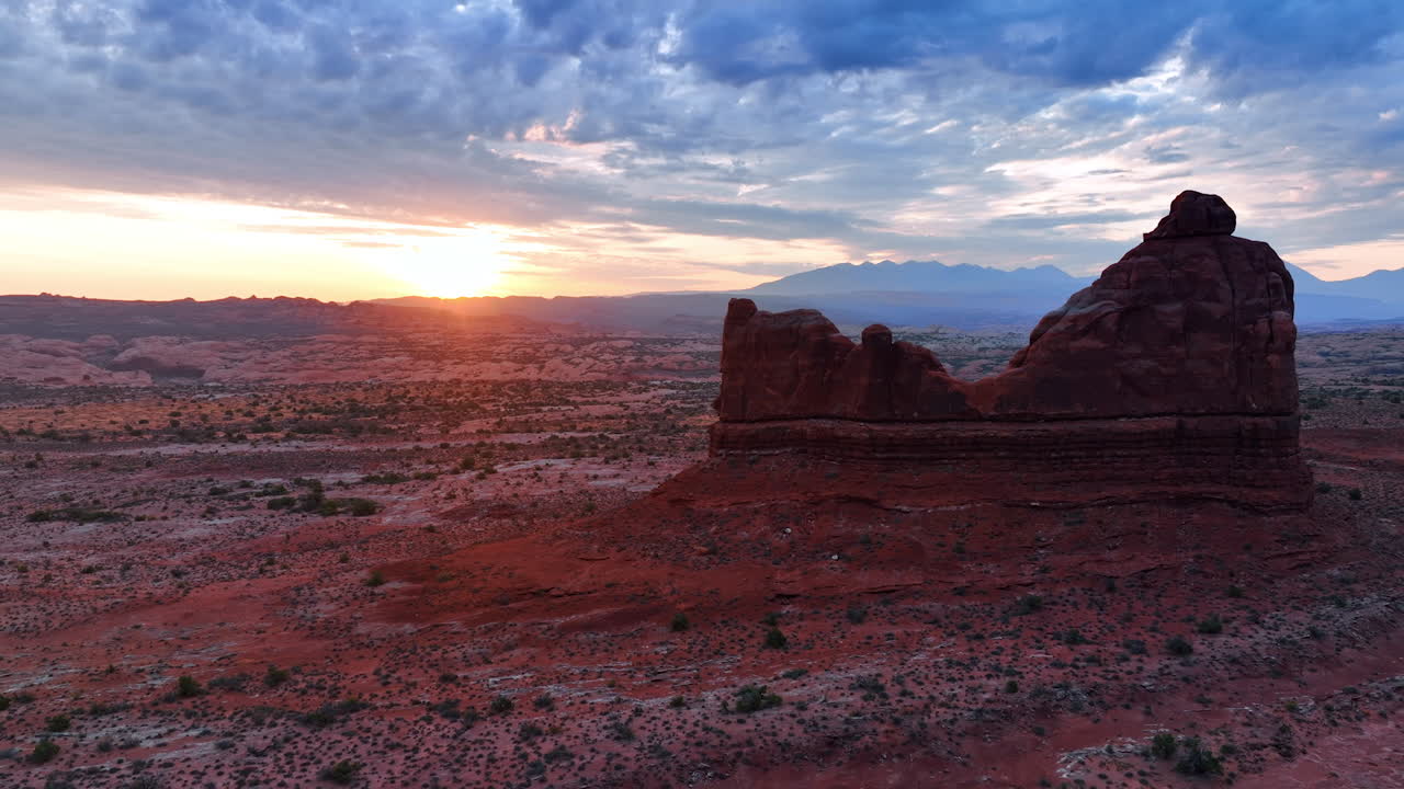 Discesa sopra il deserto arido lungo le ripide rocce a strapiombo. Un soffice cielo grigio e nuvoloso copre il paesaggio dell'Arches National Park nello Utah, USA. Filmato al tramonto