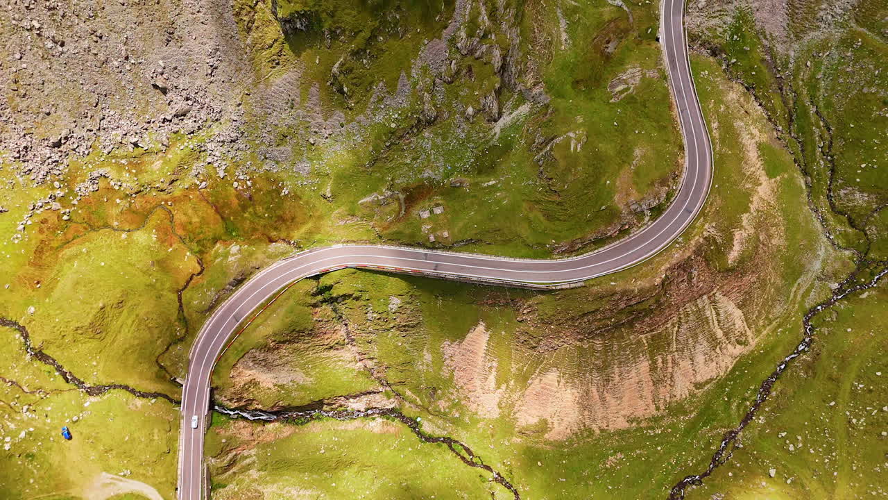 Flight above the high rock crossed by the wavy highway. Numerous cars stand or move slowly by the upper part of the Transfagarash road