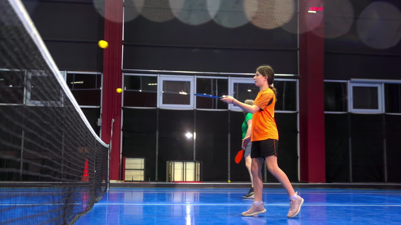 A woman and a child playing pickleball on a blue, inside court