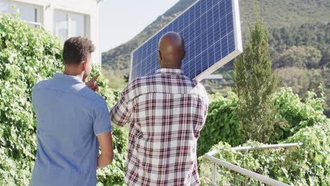 african american father holding solar panel talking to adult son in sunny garden, slow motion