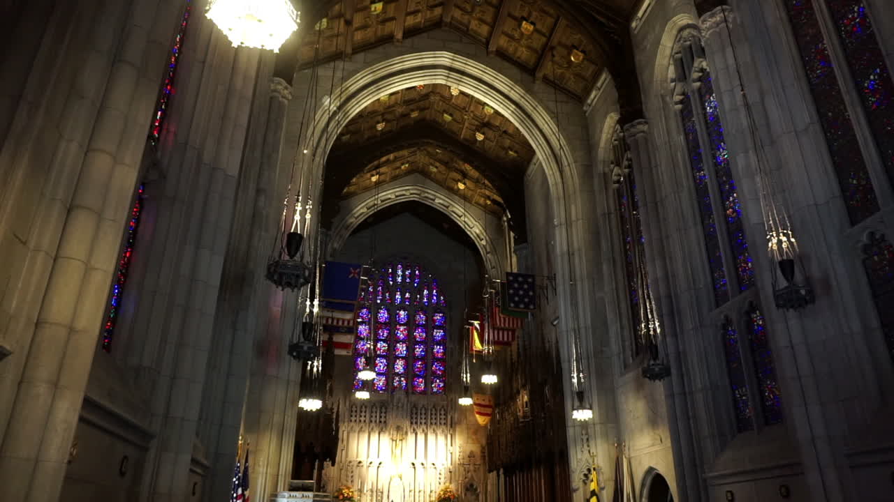 Cathedral interior with stained glass gothic windows, vaulted ceiling, carved wood ceiling panels, and flags