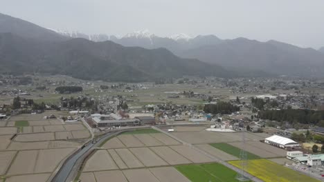 aerial view of agricultural farming fields in azumino countryside with view of kamikochi national park in background. dolly back shot