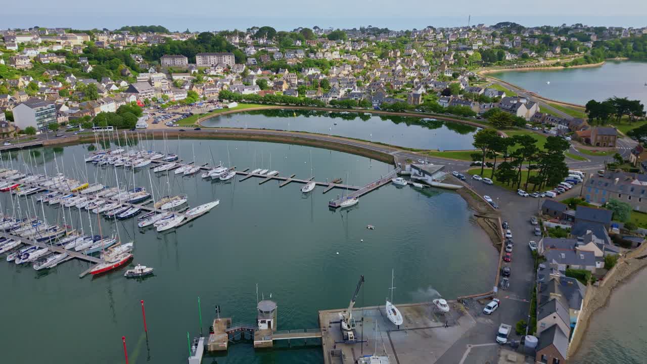 Panning backward drone movement over the marina at Perros-Guirec settlement with docked sailboats, Brittany, France.