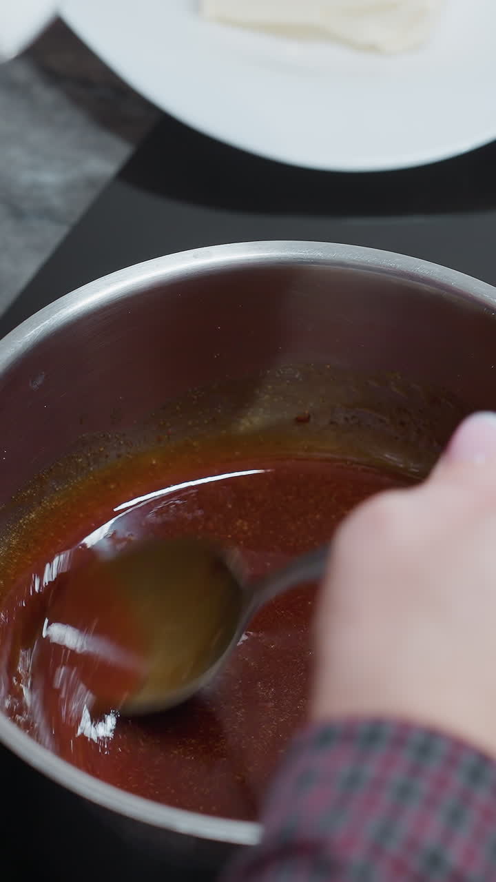 primer plano de la mano del cocinero moviendo sopa rica y sabrosa en una olla con una cuchara, un libro de cocina y equipos de cocina son parcialmente visibles en el fondo