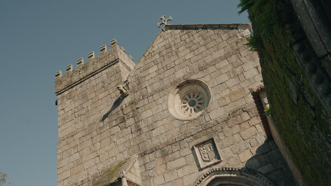 Facciata di chiesa in pietra con torre, finestra e croce su un cielo terso